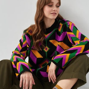 Puede incluir: Un su&eacute;ter negro con un patr&oacute;n geom&eacute;trico en tonos de rosa, naranja, verde y amarillo. El su&eacute;ter tiene mangas largas y cuello redondo.