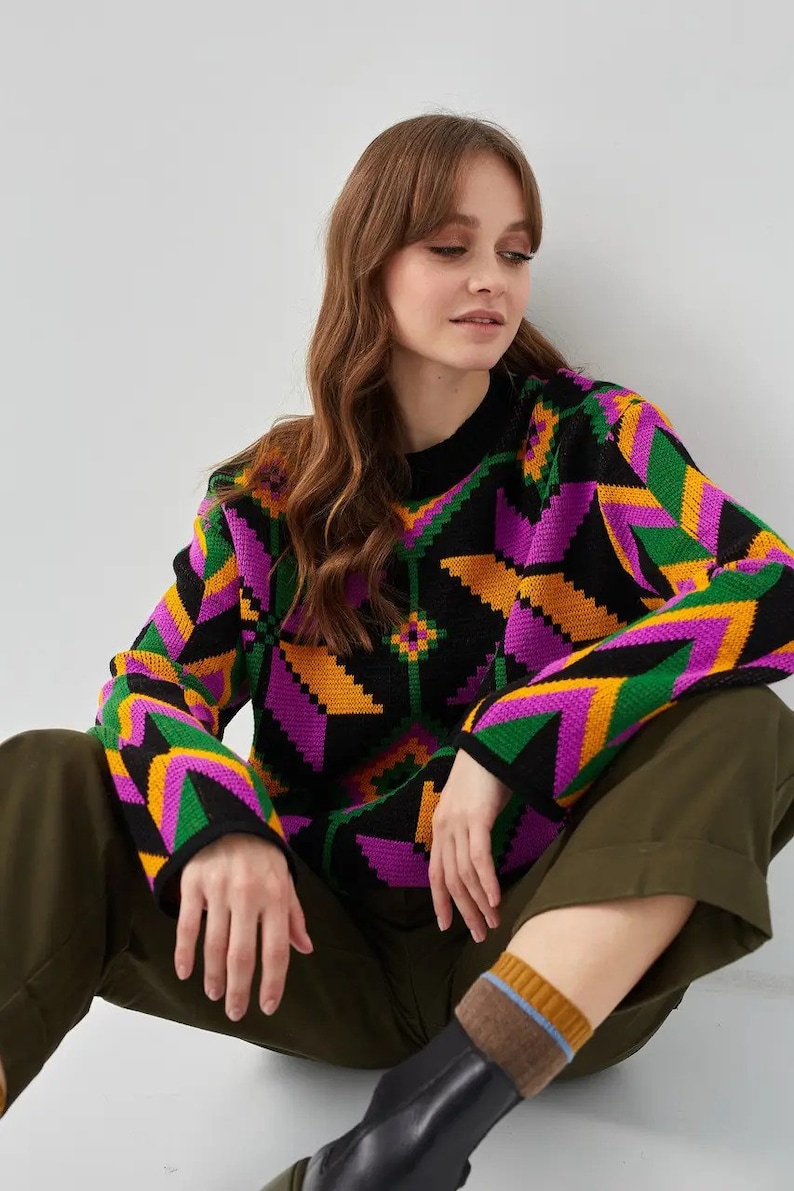 Puede incluir: Un su&eacute;ter negro con un patr&oacute;n geom&eacute;trico en tonos de rosa, naranja, verde y amarillo. El su&eacute;ter tiene mangas largas y cuello redondo.