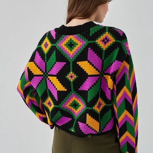 Puede incluir: Un su&eacute;ter negro con un patr&oacute;n geom&eacute;trico colorido en tonos de rosa, verde, amarillo y naranja. El su&eacute;ter tiene cuello redondo y mangas largas.