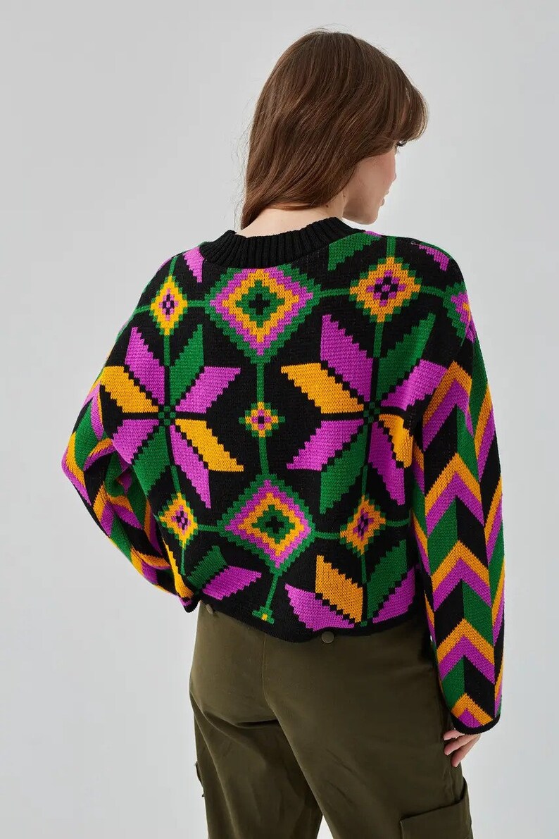 Puede incluir: Un su&eacute;ter negro con un patr&oacute;n geom&eacute;trico colorido en tonos de rosa, verde, amarillo y naranja. El su&eacute;ter tiene cuello redondo y mangas largas.