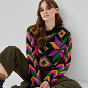 Puede incluir: Un su&eacute;ter negro con un patr&oacute;n geom&eacute;trico colorido en tonos de rosa, verde, amarillo y naranja. El su&eacute;ter tiene mangas largas y cuello redondo.