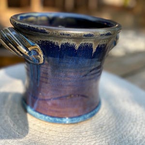 May include: A blue ceramic planter with two handles. The planter has a mottled glaze with a light blue rim.