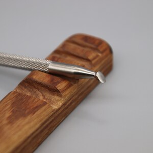 Pu&ograve; includere: Uno strumento in metallo argentato con una punta arrotondata, che riposa su un supporto in legno. Lo strumento ha un'impugnatura testurizzata ed &egrave; progettato per l'artigianato o la scultura.