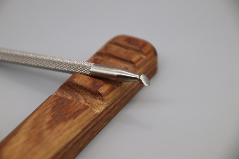 Pu&ograve; includere: Uno strumento in metallo argentato con una punta arrotondata, che riposa su un supporto in legno. Lo strumento ha un'impugnatura testurizzata ed &egrave; progettato per l'artigianato o la scultura.