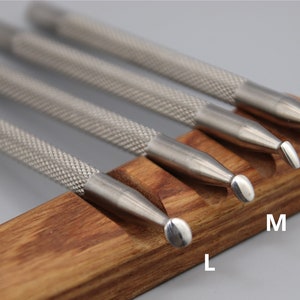Pu&ograve; includere: Set di quattro strumenti in acciaio inossidabile con punte arrotondate di diverse dimensioni, etichettati XS, S, M ed L, esposti su un supporto in legno.