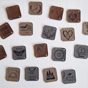 K&ouml;nnte beinhalten: Eine Sammlung von 16 quadratischen Leder-Etiketten mit verschiedenen Designs und Texten. Die Etiketten sind braun, grau und schwarz. Einige der Texte beinhalten "Your Logo", "Handmade by Gwen", "Made with Grace", "Love Never Fails" und "Knit by Alecia".