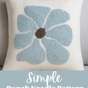 May include: A square, off-white pillow with a large, light blue flower design. The flower petals have a textured, raised appearance, and the center is brown. The text "Simple Punch Needle Pattern" is below the pillow.