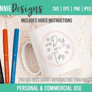 Könnte beinhalten: Eine weiße Keramiktasse mit einem rosafarbenen Kreisdesign, auf dem in schwarzer Schrift "one Day at a Time" steht. Die Tasse steht auf einer weißen Strickoberfläche mit drei Cricut Infusible Ink Stiften in Schwarz, Orange und Blau.