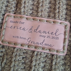 May include: A brown leather label with stitched edges. The label has the text "made for erica & daniel may 25, 2025 with love. Grandma" written in black.