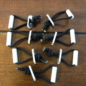 May include: Ten black paracord loops with white plastic handles and metal plates. The loops are tied with a knot and the handles are attached to the plates.