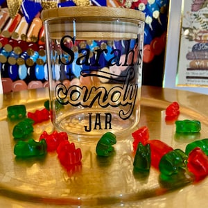 May include: A glass candy jar with a bamboo lid. The jar has a black vinyl decal that says "Sarah's candy JAR". The jar is surrounded by red and green gummy bears.
