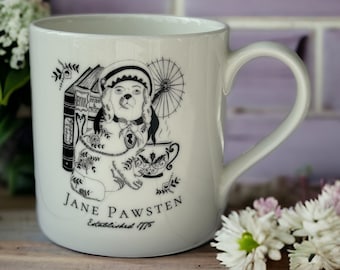 May include: White ceramic mug featuring a black and white illustration of a dog in a bonnet, with books and a teacup. The text "Jane Pawsten, Established 1775" is printed below the illustration. The mug has a curved handle and is set on a wooden surface.