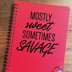May include: Red spiral bound notebook with the text "MOSTLY sweet SOMETIMES SAVAGE" in black lettering. The notebook has a small bee and flower design in the bottom right corner.