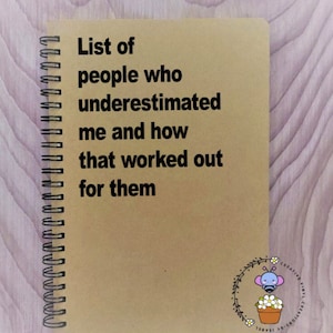 May include: A brown notebook with a spiral binding. The cover has the text "List of people who underestimated me and how that worked out for them".