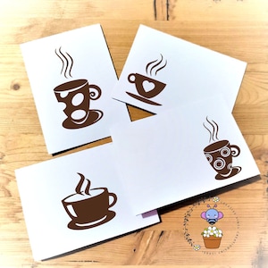 May include: Four blank white cards with brown coffee cup designs. The cards are arranged in a square shape on a wooden surface.