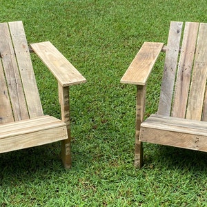 May include: Two wooden chairs made from reclaimed pallets. The chairs have a simple design with a wide seat and armrests. The chairs are sitting on a green grassy lawn.
