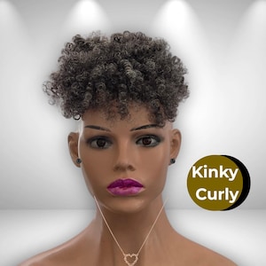 May include: A mannequin head with a short, gray, kinky curly hairpiece. The mannequin wears a heart-shaped necklace and black stud earrings. A gold and black circle graphic with the words "Kinky Curly" is on the right.