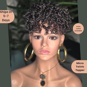 May include: A mannequin head with a short, curly, gray hair topper. The mannequin wears large gold hoop earrings and a gold necklace with a pendant. Text on the image reads "Micro Twists Topper" and "more colors Available."
