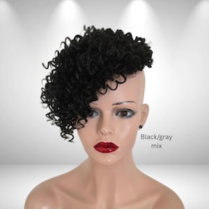 May include: A mannequin head featuring a short, curly black wig styled with a side-swept fringe and an undercut on one side. The mannequin has smooth, light-toned skin, dark eyes, and glossy red lips. The text Black/gray mix is printed on the side.