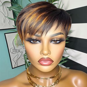May include: A short, choppy pixie wig with black and blonde highlights. The wig is styled with a side part and has a natural, textured look.