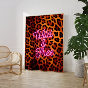 May include: A digital print with a leopard print background and the words "Wild & Free" in pink neon lettering.