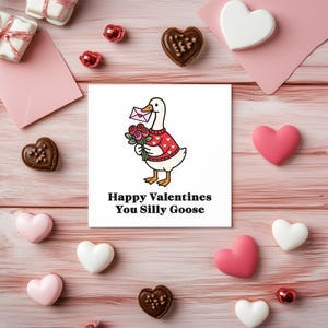 May include: A Valentine's Day-themed image featuring a card with a cartoon goose holding flowers and a letter. The card reads "Happy Valentines You Silly Goose." The image includes heart-shaped candies, gifts, and pink envelopes on a pink wooden surface.
