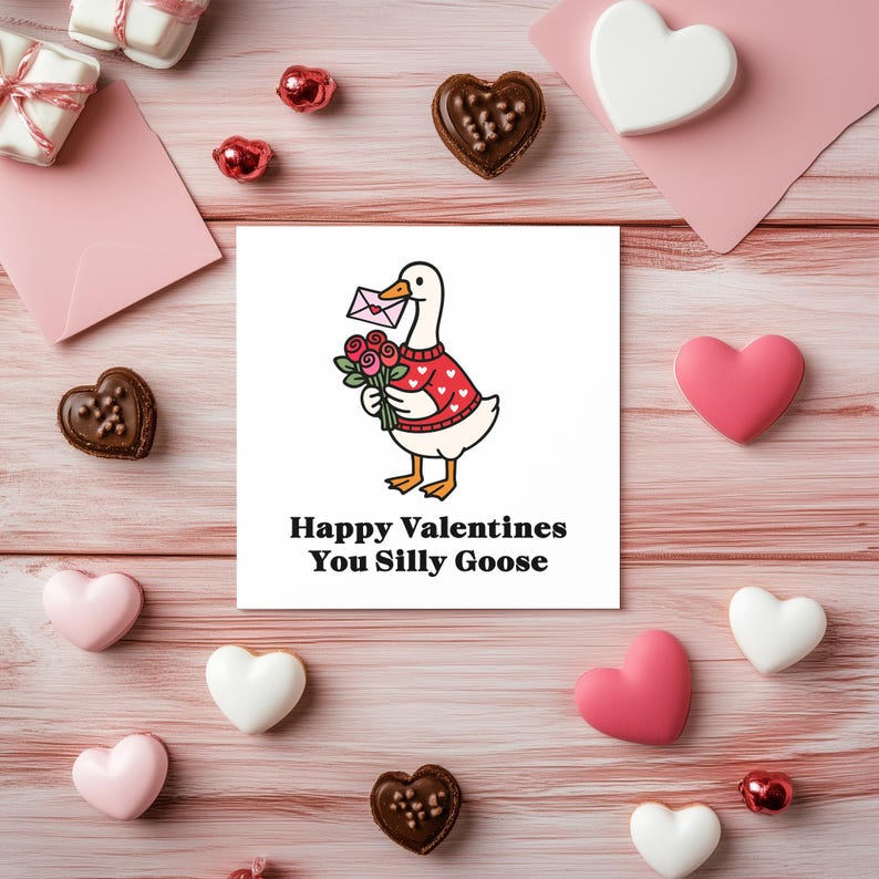 May include: A Valentine's Day-themed image featuring a card with a cartoon goose holding flowers and a letter. The card reads "Happy Valentines You Silly Goose." The image includes heart-shaped candies, gifts, and pink envelopes on a pink wooden surface.