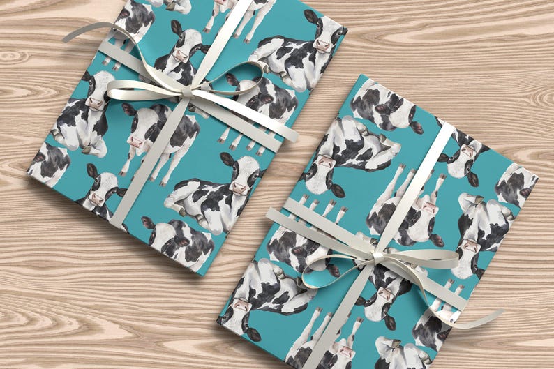 May include: Two wrapped gifts with a teal background featuring a pattern of black and white cows. The gifts are tied with white ribbon and bows. The gifts are on a light brown wooden surface.