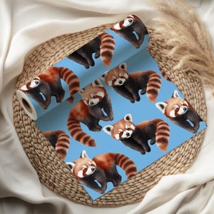 K&ouml;nnte beinhalten: Eine Rolle blaue Tapete mit einem sich wiederholenden Muster von roten Pandas. Die Pandas haben rotbraunes Fell, schwarze Beine und gestreifte Schw&auml;nze. Die Tapete wird auf einem Weidenkorb pr&auml;sentiert.