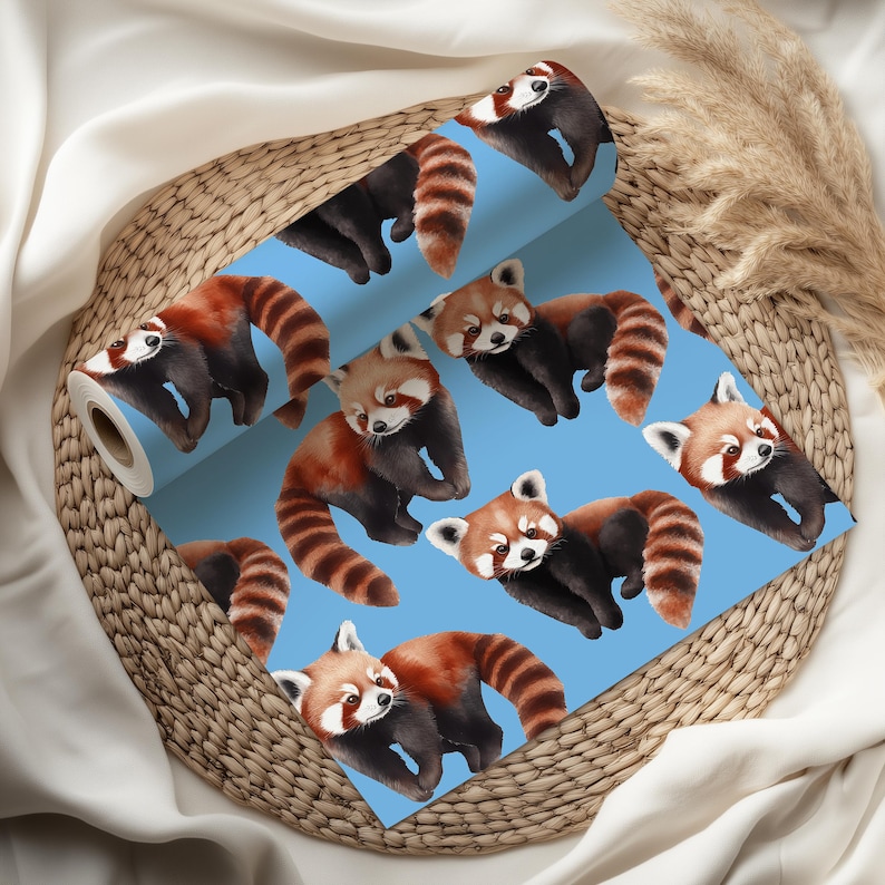 K&ouml;nnte beinhalten: Eine Rolle blaue Tapete mit einem sich wiederholenden Muster von roten Pandas. Die Pandas haben rotbraunes Fell, schwarze Beine und gestreifte Schw&auml;nze. Die Tapete wird auf einem Weidenkorb pr&auml;sentiert.