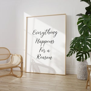May include: A white framed poster with the text "Everything Happens For a Reason" in black cursive font. The poster is hanging on a white wall in a room with a wicker chair and a potted plant.