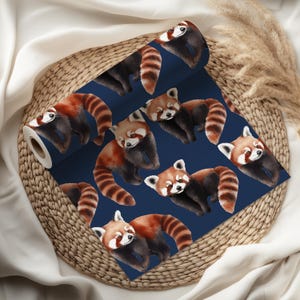 K&ouml;nnte beinhalten: Eine Tapetenrolle mit einem sich wiederholenden Muster von roten Pandas auf marineblauem Hintergrund. Die roten Pandas haben rotbraunes Fell, gestreifte Schw&auml;nze und wei&szlig;e Markierungen. Die Tapete wird auf einem Weidenkorb pr&auml;sentiert.
