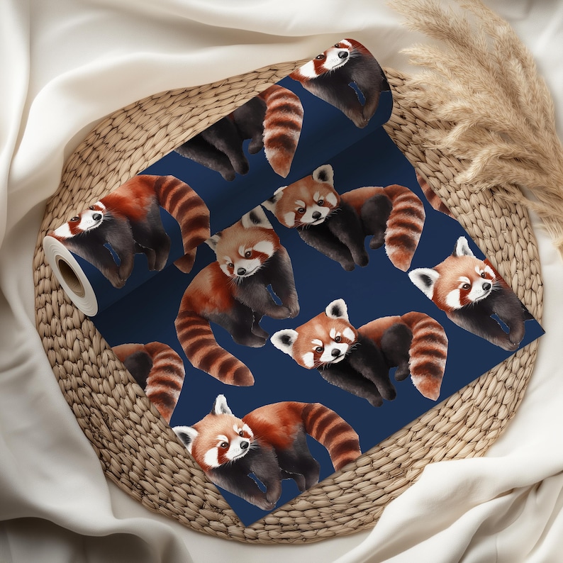 K&ouml;nnte beinhalten: Eine Tapetenrolle mit einem sich wiederholenden Muster von roten Pandas auf marineblauem Hintergrund. Die roten Pandas haben rotbraunes Fell, gestreifte Schw&auml;nze und wei&szlig;e Markierungen. Die Tapete wird auf einem Weidenkorb pr&auml;sentiert.