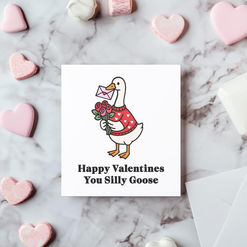May include: A square greeting card featuring a cartoon goose wearing a red sweater with white hearts, holding a bouquet of roses and an envelope. The text reads "Happy Valentines You Silly Goose". Pink heart-shaped candies surround the card.