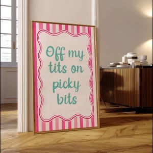 May include: A rectangular framed wall art piece featuring a white background with a pink and white vertical striped border. The center contains a wavy-edged frame enclosing the teal text: Off my tits on picky bits, written in a cursive script.