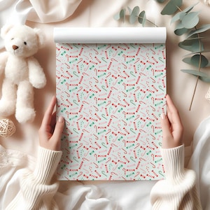 May include: A roll of wrapping paper featuring a repeating pattern of red and white candy canes, green bows, and pink hearts on a pale blue backdrop. The paper is held by a person wearing a white sweater.