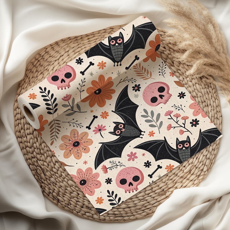 May include: A roll of patterned fabric featuring a Halloween theme. The design includes black bats, pink skulls, orange and pink flowers, and bone accents on a cream background. The fabric is displayed on a woven basket.