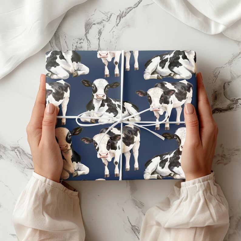 Wrapping paper with hand-painted black and white cows in seated and standing poses, tied with string on a marble background.