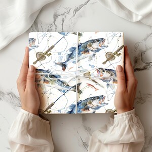 Puede incluir: Una caja de regalo rectangular envuelta en papel blanco con un patr&oacute;n de acuarela repetitivo de peces azules y plateados, ca&ntilde;as de pescar y redes peque&ntilde;as, atada con un cordel blanco fino en un patr&oacute;n de cruz simple.