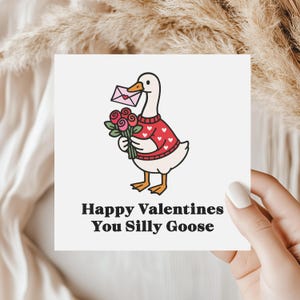 May include: A square greeting card featuring a cartoon goose wearing a red sweater with white hearts, holding a bouquet of roses and a pink envelope. The text reads "Happy Valentines You Silly Goose."