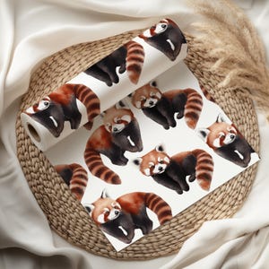 K&ouml;nnte beinhalten: Eine Tapetenrolle mit einem sich wiederholenden Muster von roten Pandas. Die Pandas haben rotbraunes Fell, schwarze Markierungen und gestreifte Schw&auml;nze, vor einem wei&szlig;en Hintergrund. Die Tapete wird auf einem Weidenkorb pr&auml;sentiert.