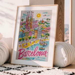 May include: A framed art print featuring a colorful illustration of Barcelona, Spain. The artwork depicts the Sagrada Familia, buildings, beach, and boats. The word "Barcelona" is written in pink script across the bottom.