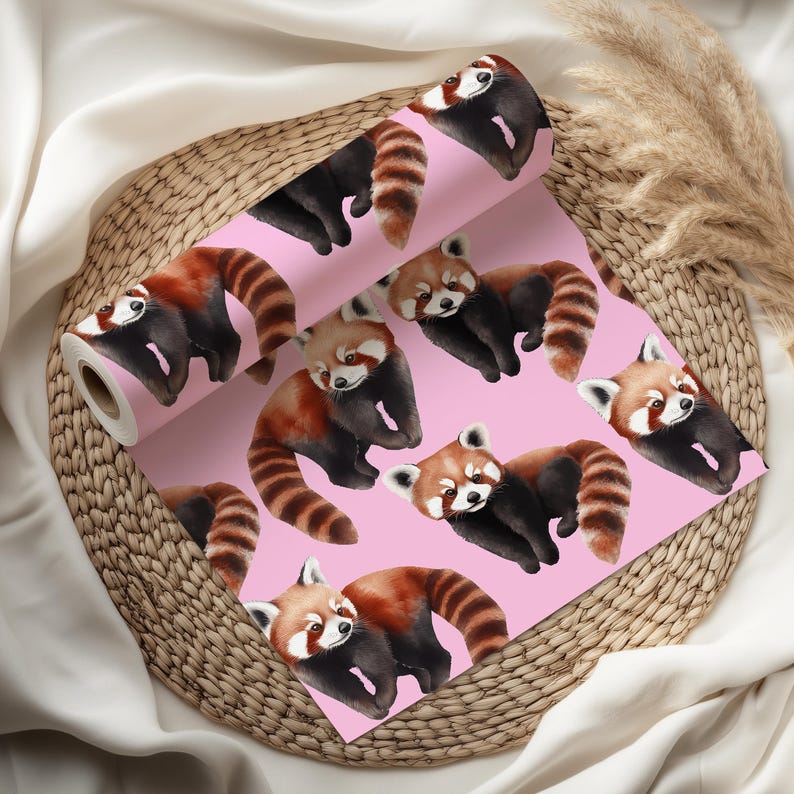 K&ouml;nnte beinhalten: Eine Rolle rosa Tapete mit einem sich wiederholenden Muster von roten Pandas. Die roten Pandas haben rotbraunes Fell, schwarze Beine und gestreifte Schw&auml;nze. Die Tapete wird auf einem Weidenkorb pr&auml;sentiert.