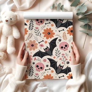 Wrapping paper featuring black bats, pink skulls, and orange flowers with leafy accents on a beige background, ideal for Halloween or gothic gifts.