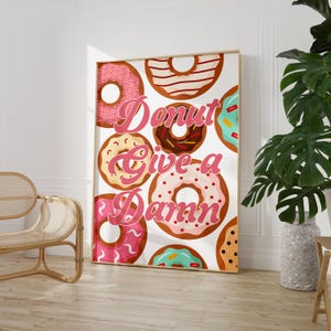 May include: A white background with a pink and white donut pattern. The text "Donut Give a Damn" is written in pink cursive letters.