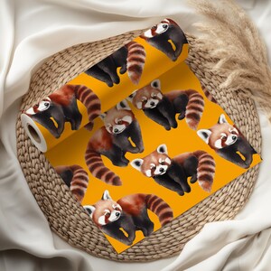 K&ouml;nnte beinhalten: Eine Rolle gelbe Tapete mit einem sich wiederholenden Muster von roten Pandas. Die roten Pandas haben braunes und schwarzes Fell mit gestreiften Schw&auml;nzen. Die Tapete wird auf einem Weidenkorb pr&auml;sentiert.