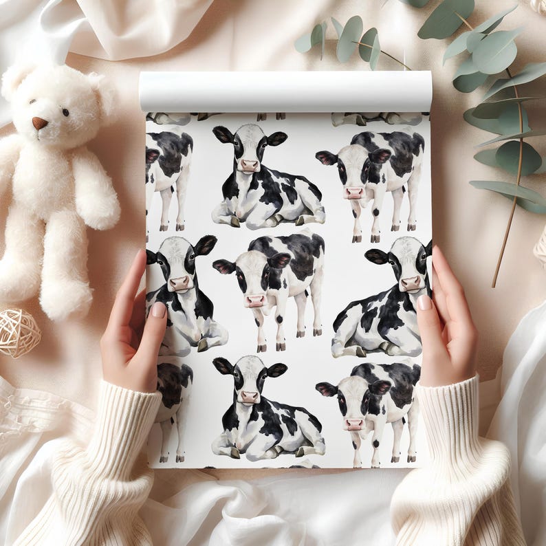 Wrapping paper with hand-painted black and white cows in seated and standing poses, tied with string on a marble background.