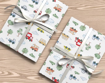 May include: Two gift boxes wrapped in white paper with a colorful pattern of cars, trucks, and buses. The boxes are tied with white ribbon.
