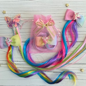 May include: Three colorful hair clips with unicorn charms and rainbow hair extensions. The clips are pink, blue, and green with a white bow and a unicorn charm on each. The hair extensions are a mix of pink, blue, green, and yellow.