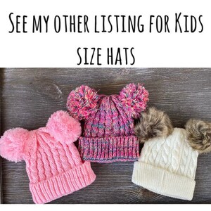 May include: Three knitted winter hats with pom-poms. One is pink, one is multicolored, and one is white. The hats are displayed on a dark wood surface. Text at the top reads: "SEE MY OTHER LISTING FOR KIDS SIZE HATS."